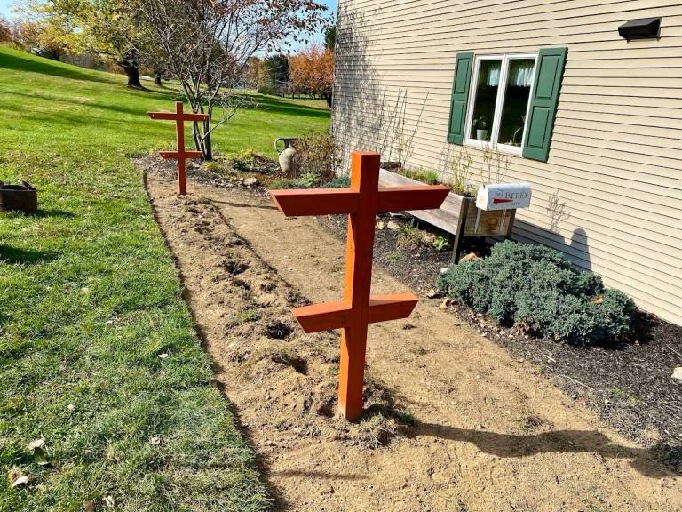 Wooden raspberry trellis posts and a prepared planting bed beside a house.